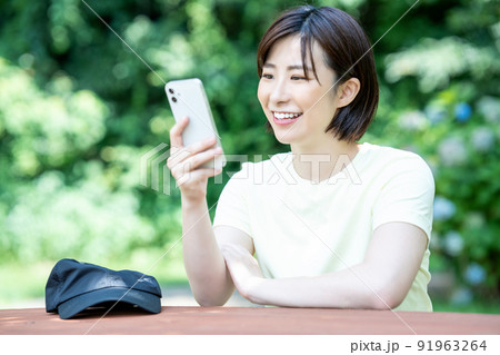 新緑の公園のテーブルでスマホを使う女性 91963264
