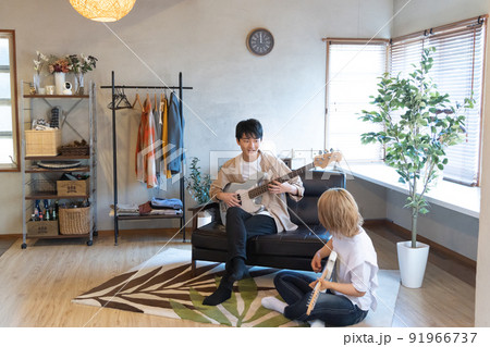 リビングでギターとベースを弾く若い男女 リビングでギターとベースを弾く若い男女 91966737