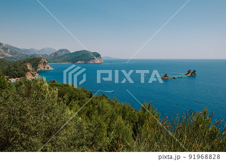 Picturesque view on rocks on a sunny day from the sea. Budva riviera, Montenegro. Aerial view of Sveti Nikola, Budva island, Montenegro. Hawaii beach, umbrellas and bathers and crystal clear waters 91968828