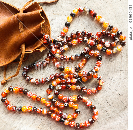 Sunny beads of amber fireplace faceted agate with leather jewelry pouch bag on rustic background Sunny beads of amber fireplace faceted agate with leather jewelry pouch bag on rustic background 91969455