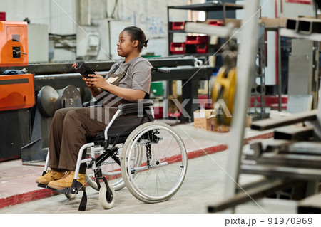 African worker with disability sitting in wheelchair and working at machine with remote control African worker with disability sitting in wheelchair and working at machine with remote control 91970969