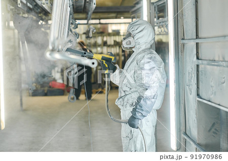 Coveralls worker with spray gun painting steel parts in painting chamber Coveralls worker with spray gun painting steel parts in painting chamber 91970986