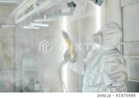Worker in protective suit working with spray gun to paint metal details at factory 91970988