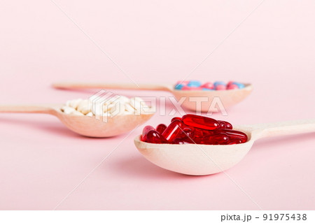 Vitamin capsules in a spoon on a colored background. Pills served as a healthy meal. Red soft gel vitamin supplement capsules on spoon 91975438