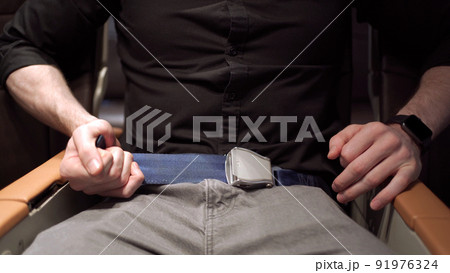 Unrecognizable businessman passenger onboard fastening a seat belt while sitting in the airplane. Safety regulation and instruction in commercial airline flight concept. 91976324