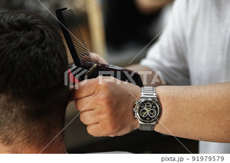 Barber guy gives a haircut to a bearded man sitting in a chair in a barbershop Barber guy gives a haircut to a bearded man sitting in a chair in a barbershop 91979579