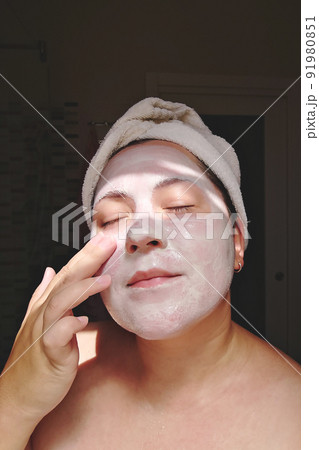 Candid woman applies mask of clay, minerals and salts to her face in home bathroom. Self skincare 91980851