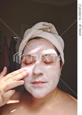 Candid woman applies mask of clay, minerals and salts to her face in home bathroom. Self skincare Candid woman applies mask of clay, minerals and salts to her face in home bathroom. Self skincare 91980852