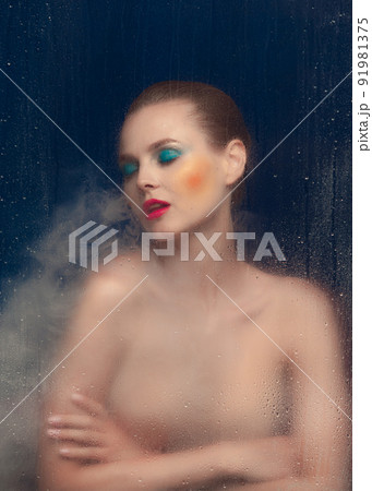 Portrait of beautiful woman with bright makeup posing in underwear isolated over dark blue background. Foggy glass effect. Blue eyeshadows 91981375