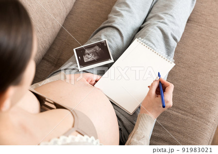 Top view caring future mother writing diary with ultrasound. pregnant woman tummy making notes feeling during pregnancy or creating scrapbook 91983021