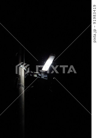 電柱に設置されたライトに多数の虫が群がっている夏の夜間の屋外の光景を高感度で撮影した画像 91983419
