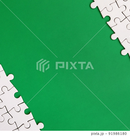 Fragment of a folded white jigsaw puzzle on the background of a green plastic surface. Texture photo with copy space for text Fragment of a folded white jigsaw puzzle on the background of a green plastic surface. Texture photo with copy space for text 91986180