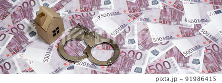 Scam with real estate. Cheating when buying or renting a house. Punishment for deception. A toy house with handcuffs on a many 500 purple euro banknotes 91986415