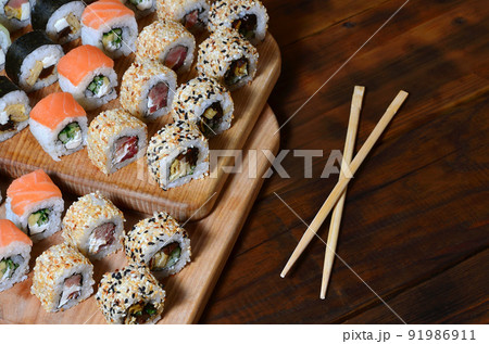 A detailed shot of a set of Japanese sushi rolls and a device for their use chopsticks , which are located on a wooden cutting board on a table in the kitchen of a sushi bar A detailed shot of a set of Japanese sushi rolls and a device for their use chopsticks , which are located on a wooden cutting board on a table in the kitchen of a sushi bar 91986911