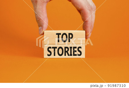 Top stories symbol. Concept words Top stories on wooden blocks on a beautiful orange table orange background. Businessman hand. Business story and top stories concept, copy space. Top stories symbol. Concept words Top stories on wooden blocks on a beautiful orange table orange background. Businessman hand. Business story and top stories concept, copy space. 91987310