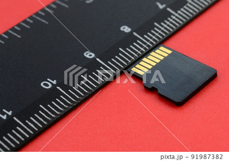 Small micro SD memory card lie on a red background next to a black ruler. A small and compact data and information store Small micro SD memory card lie on a red background next to a black ruler. A small and compact data and information store 91987382