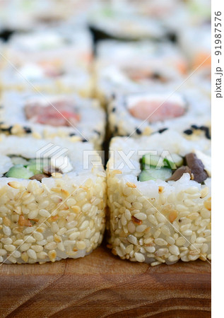 Close-up of a lot of sushi rolls with different fillings lie on a wooden surface. Macro shot of cooked classic Japanese food with a copy space Close-up of a lot of sushi rolls with different fillings lie on a wooden surface. Macro shot of cooked classic Japanese food with a copy space 91987576