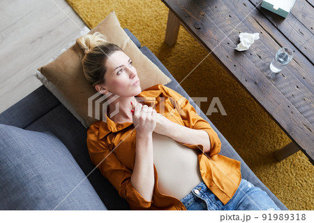 High angle view of serious beautiful young woman in orange blouse lying on sofa in psychoanalysts office and rubbing hands nervously 91989318