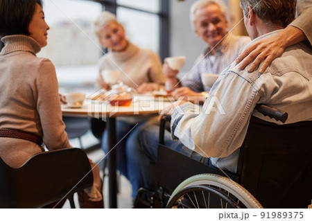 Group of senior people visiting friend in wheelchair: they drinking tea and chatting at home Group of senior people visiting friend in wheelchair: they drinking tea and chatting at home 91989375