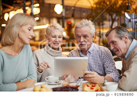 Group of content curious senior friends in casual outfits sitting at table in cafe with wi-fi and surfing net on tablet together Group of content curious senior friends in casual outfits sitting at table in cafe with wi-fi and surfing net on tablet together 91989890