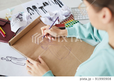 Over shoulder view of fashion designer sitting at table and brainstorming about dress design while drawing sketch Over shoulder view of fashion designer sitting at table and brainstorming about dress design while drawing sketch 91990908