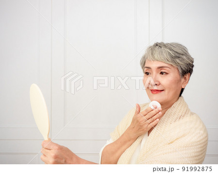Portrait of mature aged asian woman 50s touching face skin looking in mirror reflection. Smiling mature old lady pampering, healthy moisturized skin care, aging beauty, skincare treatment cosmetics Portrait of mature aged asian woman 50s touching face skin looking in mirror reflection. Smiling mature old lady pampering, healthy moisturized skin care, aging beauty, skincare treatment cosmetics 91992875