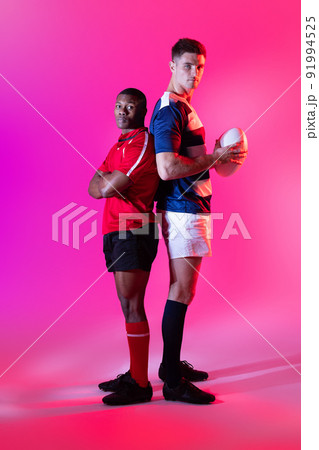 Portrait of diverse male rugby players with rugby ball over pink lighting Portrait of diverse male rugby players with rugby ball over pink lighting 91994525