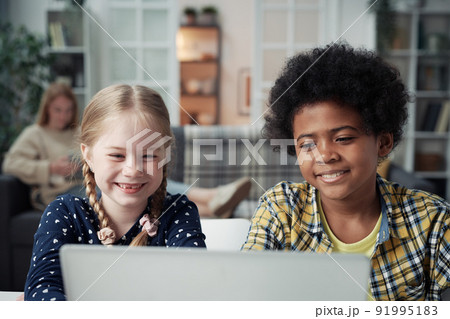 Multiethnic kids watching funny video on laptop while their mom resting in background 91995183