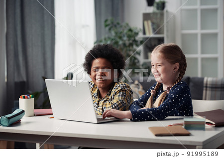 Happy multiethnic children using laptop together and browsing the net while sitting at table at home 91995189