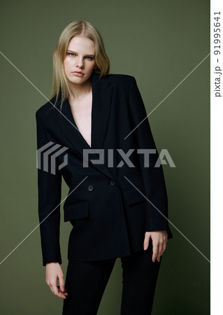 A stunning elegant girl in a black suit leans forward and poses professionally on a green background in the studio. The concept of advertising for designer brands A stunning elegant girl in a black suit leans forward and poses professionally on a green background in the studio. The concept of advertising for designer brands 91995641