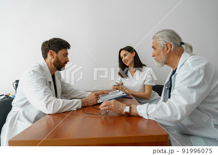 Group of doctors sitting at meeting table in conference room during medical seminar Group of doctors sitting at meeting table in conference room during medical seminar 91996075