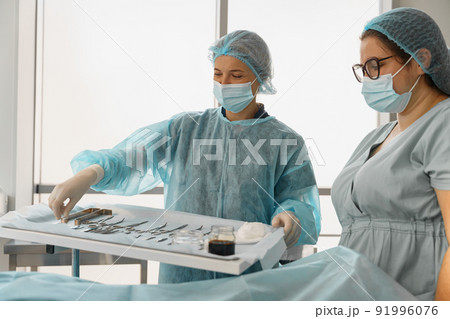 Doctor and nurse examining table with surgical instruments before the operation 91996076
