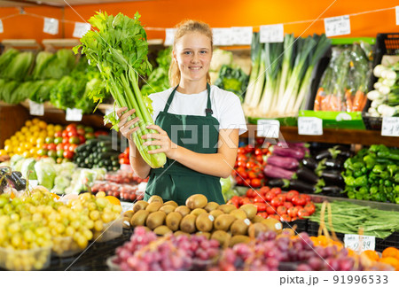 Portrait of a positive girl who works part-time as a trainee saleswoman, holding celery 91996533