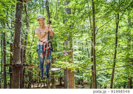 Happy women girl female gliding climbing in extreme road trolley zipline in forest on carabiner safety link on tree to tree top rope adventure park. Family weekend children kids activities concept Happy women girl female gliding climbing in extreme road trolley zipline in forest on carabiner safety link on tree to tree top rope adventure park. Family weekend children kids activities concept 91998549