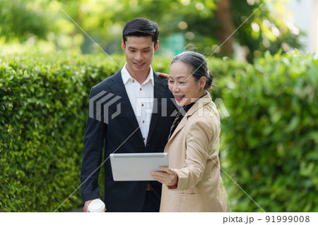 Portrait of Asian Senior Business woman and young business man discussing about project by digital tablet. Account and Finance concept. Portrait of Asian Senior Business woman and young business man discussing about project by digital tablet. Account and Finance concept. 91999008
