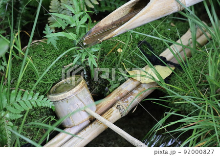 緑の植物と竹製のつくばいと柄杓と苔の生えた石製の手水鉢のある風景 92000827