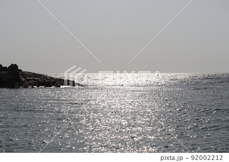 キラキラ光る海面と岩場の突堤と水平線と霞む青空のある風景 92002212