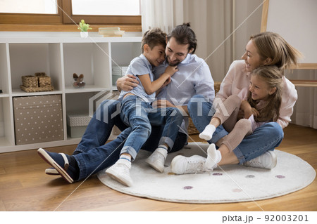 Joyful happy young parents cuddling, tickling two excited giggling kids Joyful happy young parents cuddling, tickling two excited giggling kids 92003201