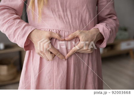Pregnant woman makes heart shape with fingers on belly, closeup Pregnant woman makes heart shape with fingers on belly, closeup 92003668