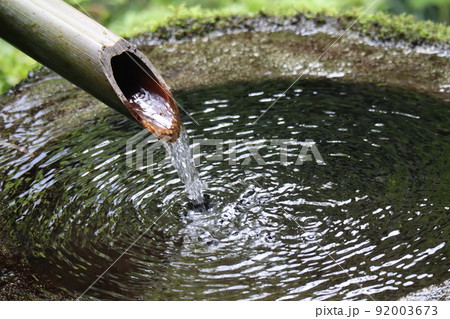 竹製のつくばいから流れる水が波紋を広げる水面の石製の手水鉢のある風景 92003673