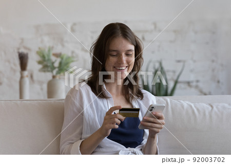 Woman sit on sofa make payment use card and smartphone 92003702
