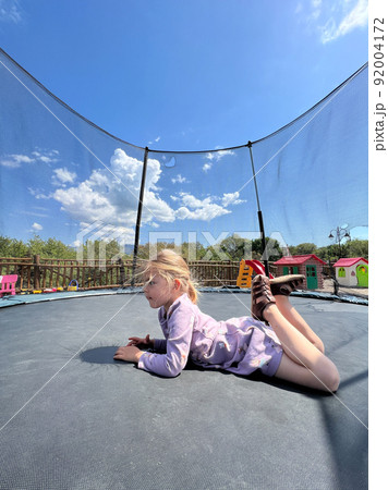 Little girl lying on her stomach on a trampoline 92004172