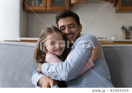 Little daughter cuddles tightly her stepdad seated on sofa 92004354