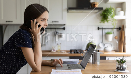 Positive busy young freelance girl talking on telephone at laptop Positive busy young freelance girl talking on telephone at laptop 92004580