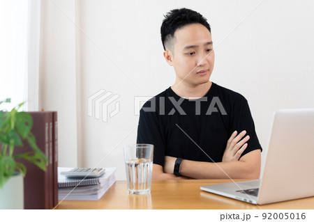 Asian young student using laptop computer for online study at home in the new normal lifestyle. Stressful Asian man making a video conference and meeting while staying at home. Asian young student using laptop computer for online study at home in the new normal lifestyle. Stressful Asian man making a video conference and meeting while staying at home. 92005016