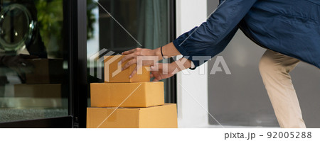 Asian postman with a hygiene protective face mask picking up a parcel package or parcel box from the truck for deliver to customer's door. New Normal concept during covid-19 or coronavirus pandemic 92005288