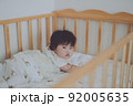 ベビーベッドから静かにこちらを見つめる赤ちゃん 92005635