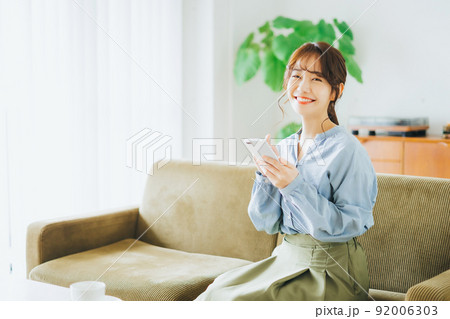 ソファに座ってスマホを使う女性 ソファに座ってスマホを使う女性 92006303