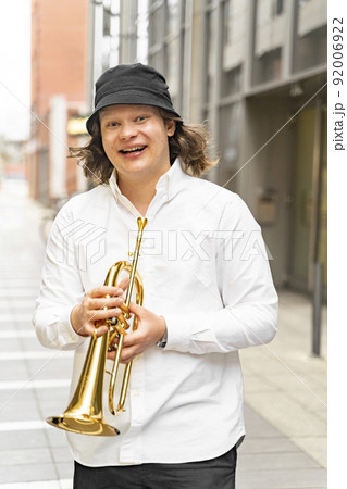 Young caucasian long-haired well-dressed cheerful man playing trumpet outdoor Young caucasian long-haired well-dressed cheerful man playing trumpet outdoor 92006922