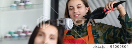 Cheerful hairdresser using hairdryer for treatment with clients hairstyle Cheerful hairdresser using hairdryer for treatment with clients hairstyle 92009304